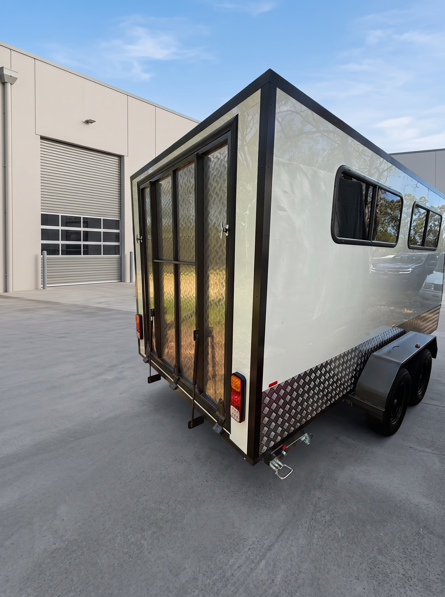 Rear three-quarter view of the MotoCampers 002 enclosed trailer with side windows and checkerplate guards